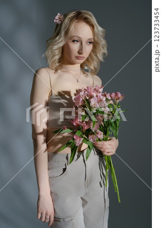 Young woman poses with bouquet of pink flowers in soft lighting indoors 123733454