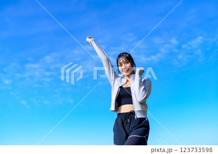ウォーキングしながら青空に向かって可愛くガッツポーズする若い女性　ワークアウト　 123733598