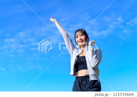 ウォーキングしながら青空に向かって可愛くガッツポーズする若い女性　ワークアウト　トリミングアップ 123733609