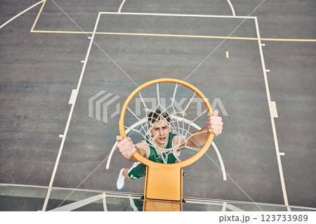 Portrait of basketball player hanging on net on a basketball court. Young man playing basketball outside doing slam dunk and jumping to score a point. Motivation to win and have fun in sports game 123733989