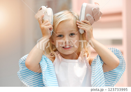 Children, fashion and clothes with shoes in girl hands against her head while shopping in a retail store. Kids, cute and choice with a female child deciding what shoe to buy for her wardrobe 123733995