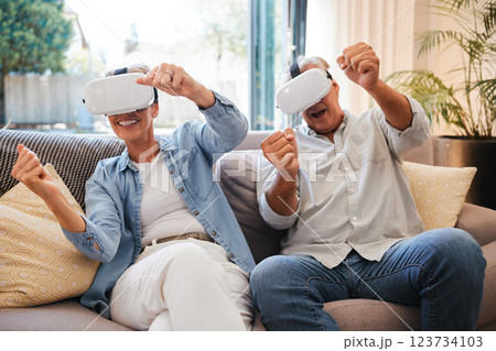 Senior couple with futuristic virtual reality technology on the sofa in their home. Retired man and woman using tech, digital gadgets and vr headset for 3d games and entertainment in the metaverse 123734103