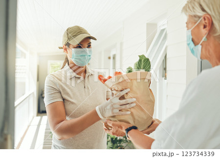 Delivery, covid and logistics with a woman courier giving grocery shopping to a customer in her home. Ecommerce, retail and service with a distribution employee fulfilling an order in the pandemic 123734339