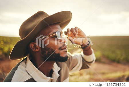 Sustainability, farm and agriculture with a black man or cowboy farmer chewing straw in a grass field or meadow. Sustainable, farming and sustainable with a young male working in organic ecology 123734591