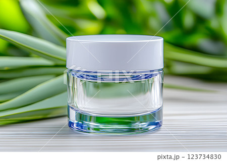 Clear cosmetic jar surrounded by green leaves, ideal for organic skin serum and therapy products, promoting a fresh spa experience with essential oils 123734830