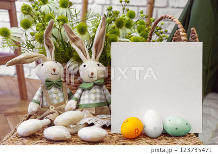 Decorative toy bunnies with colorful Easter eggs and square white blank cardboard with copy space 123735471