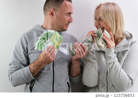 Couple holding money man and woman are sitting on a couch, holding a stack of money. The man is smiling and the woman is looking at him with a surprised expression. Scene is lighthearted and playful 123736653