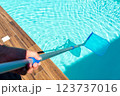 Close-up of skimmer net cleaning turquoise water in swimming pool with wooden deck 123737016