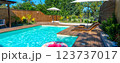 Modern backyard swimming pool with turquoise water, wooden deck, lounge chairs, umbrellas, and pink inflatable ring 123737017