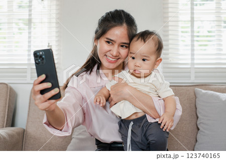 Smiling mother holding her baby while taking a selfie in a bright and cozy living room setting. 123740165