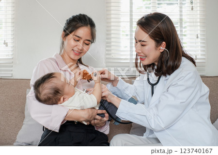 Smiling pediatrician interacting with mother and baby during a home visit, promoting health and wellness in a cozy living room. Smiling pediatrician interacting with mother and baby during a home visit, promoting health and wellness in a cozy living room. 123740167