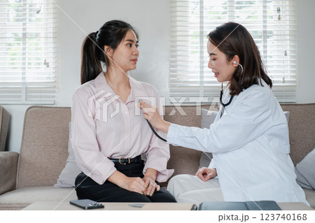 Female doctor using a stethoscope to examine a patient in a cozy living room environment, highlighting home healthcare. 123740168