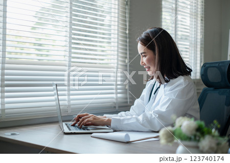 A professional woman in a white coat working on a laptop in a bright office setting, showcasing productivity and modern work environments. 123740174