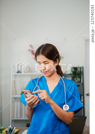 A nurse in blue scrubs with a stethoscope using a smartphone in a medical office environment. A nurse in blue scrubs with a stethoscope using a smartphone in a medical office environment. 123740191