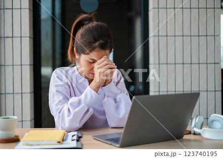 A young woman sits at a desk with a laptop, appearing stressed and deep in thought, in a modern office environment. A young woman sits at a desk with a laptop, appearing stressed and deep in thought, in a modern office environment. 123740195