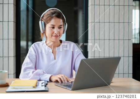 Young woman wearing headphones, working on a laptop in a modern office. Ideal for themes of remote work, technology, and productivity. 123740201