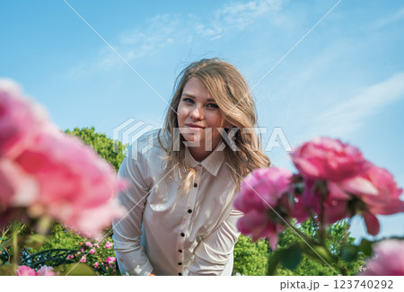 Young woman in a garden poses amidst blooming roses on a sunny day with blue sky in the background 123740292