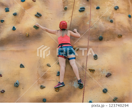 Young climber ascends a rock wall during a summer day at an outdoor adventure park in a vibrant setting 123740294