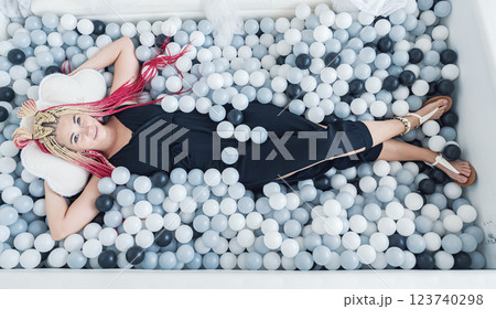 Young woman relaxes in a playful ball pit filled with monochrome spheres and a cloud pillow 123740298