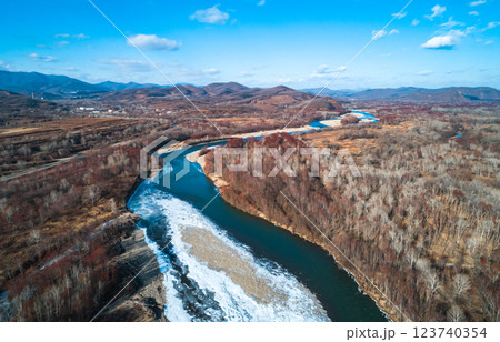 Winding river flows through a scenic valley with bare trees and mountains in the backdrop during early spring. The 123740354