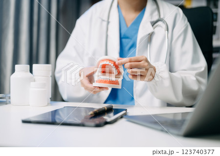 Dentist sitting at table with jaw samples tooth model and working with tablet and laptop in dental clinic. 123740377