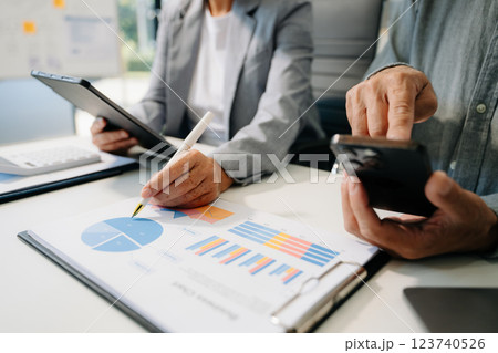 Business documents on office table with smart phone and laptop and two colleagues discussing data 123740526