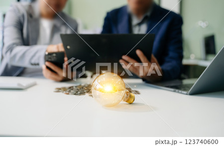 Showcasing innovation and finance. Business professionals with a glowing light bulb, coins, and digital tools symbolize 123740600