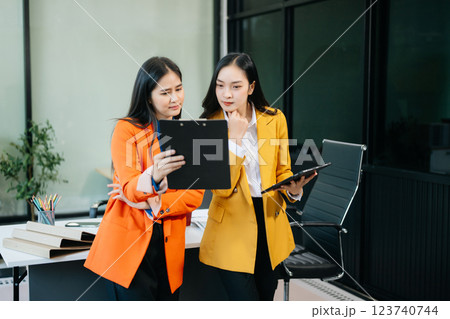 Professional women smiling confidently, collaborating with a tablet and clipboard in a modern office. 123740744