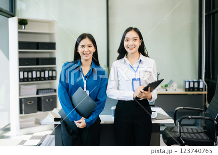 Professional women smiling confidently, collaborating with a tablet and clipboard in a modern office. 123740765