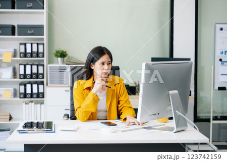 Young Asian businesswoman working with working notepad, tablet and laptop documents talking 123742159