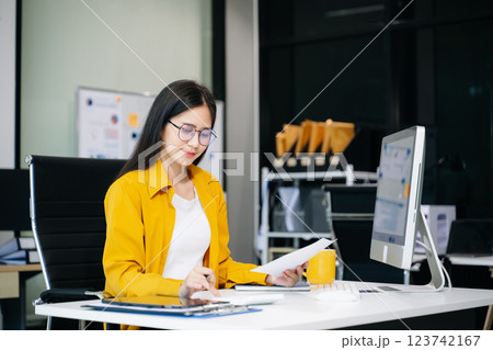 Young Asian businesswoman working with working notepad, tablet and laptop documents talking 123742167