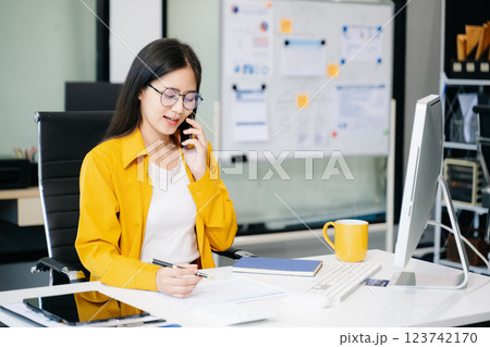 Young Asian businesswoman working with working notepad, tablet and laptop documents talking 123742170