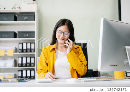 Young Asian businesswoman working with working notepad, tablet and laptop documents talking 123742171