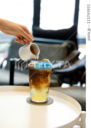 Hand pouring coffee into a cup of colorful creation beverage on table by the window. 123743953