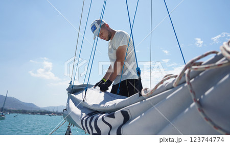 Male captain on deck of sailboat unpacking sails pulling zipper 123744774