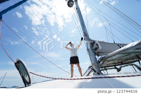 Male captain on deck of sailboat opening sails pulling the rope 123744816