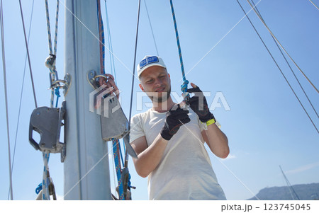 Male captain on deck of sailboat opening sails pulling the rope Male captain on deck of sailboat opening sails pulling the rope 123745045