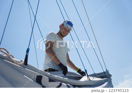 Male captain on deck of sailboat unpacking sails pulling zipper Male captain on deck of sailboat unpacking sails pulling zipper 123745123