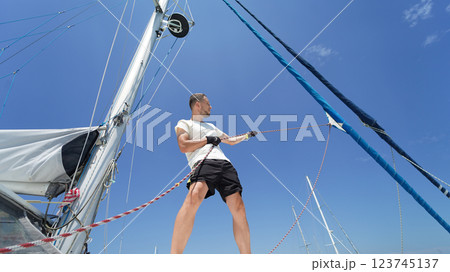 Male captain on deck of sailboat opening sails pulling the rope Male captain on deck of sailboat opening sails pulling the rope 123745137