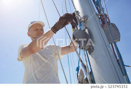 Male captain on deck of sailboat opening sails pulling the rope 123745151
