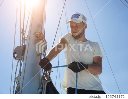 Male captain on deck of sailboat opening sails pulling the rope 123745172