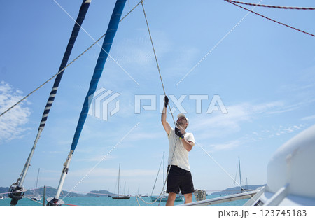 Male captain on deck of sailboat opening sails pulling the rope Male captain on deck of sailboat opening sails pulling the rope 123745183