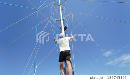 Male captain climbing mast of sailboat to check sails 123745195