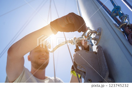 Male captain on deck of sailboat opening sails pulling the rope Male captain on deck of sailboat opening sails pulling the rope 123745232