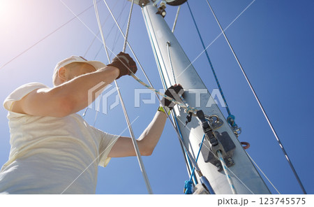 Male captain on deck of sailboat opening sails pulling the rope 123745575