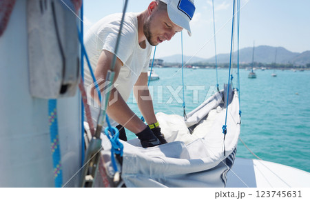 Male captain on deck of sailboat unpacking sails pulling zipper Male captain on deck of sailboat unpacking sails pulling zipper 123745631
