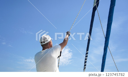 Male captain on deck of sailboat opening sails pulling the rope 123745782