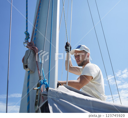 Male captain on deck of sailboat opening sails pulling the rope 123745920