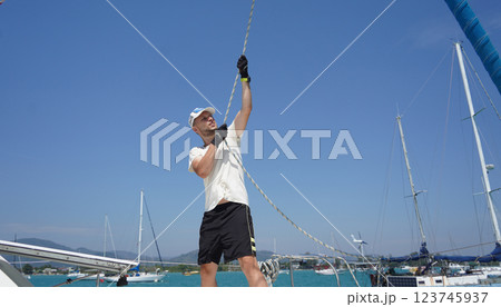 Male captain on deck of sailboat opening sails pulling the rope Male captain on deck of sailboat opening sails pulling the rope 123745937