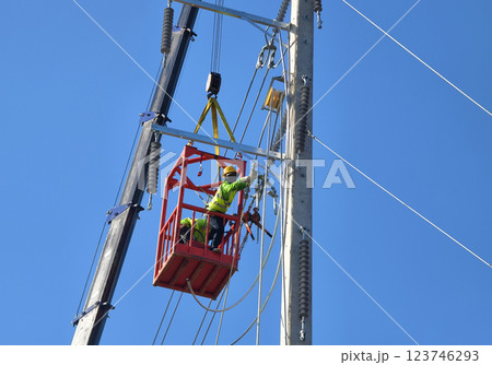 Men in work clothes and hard hats are installing high-voltage wires on a power pole 123746293